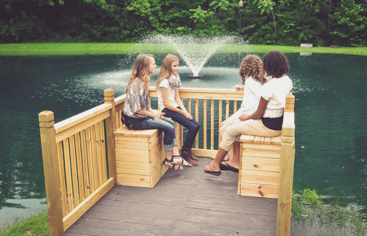 Teen girls smiling and sitting next to a pond