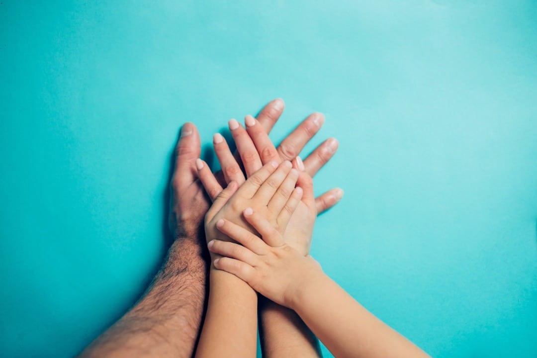 Four hands representing multiple generations stacked on top of each other on a light blue background.