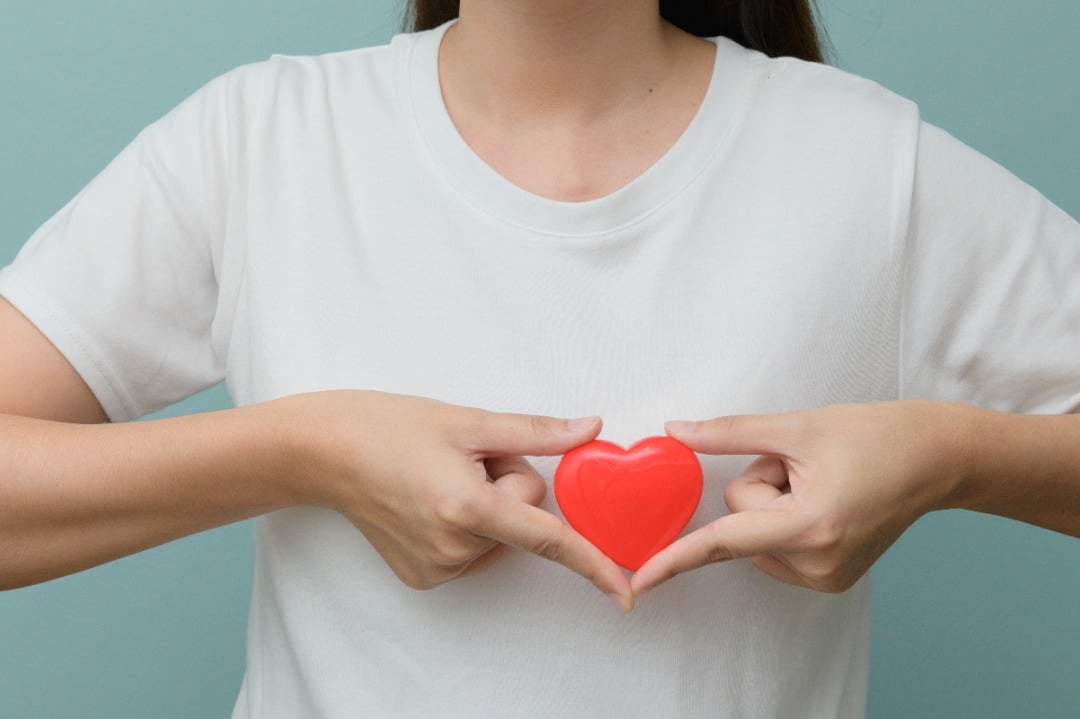 Woman in white t-shirt holds a red heart in front of her chest.