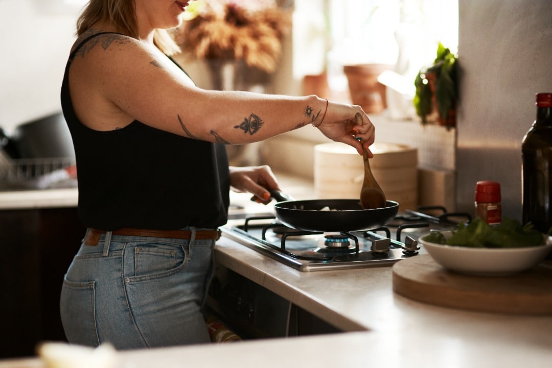 Woman with tattooed arms cooking at the stove.