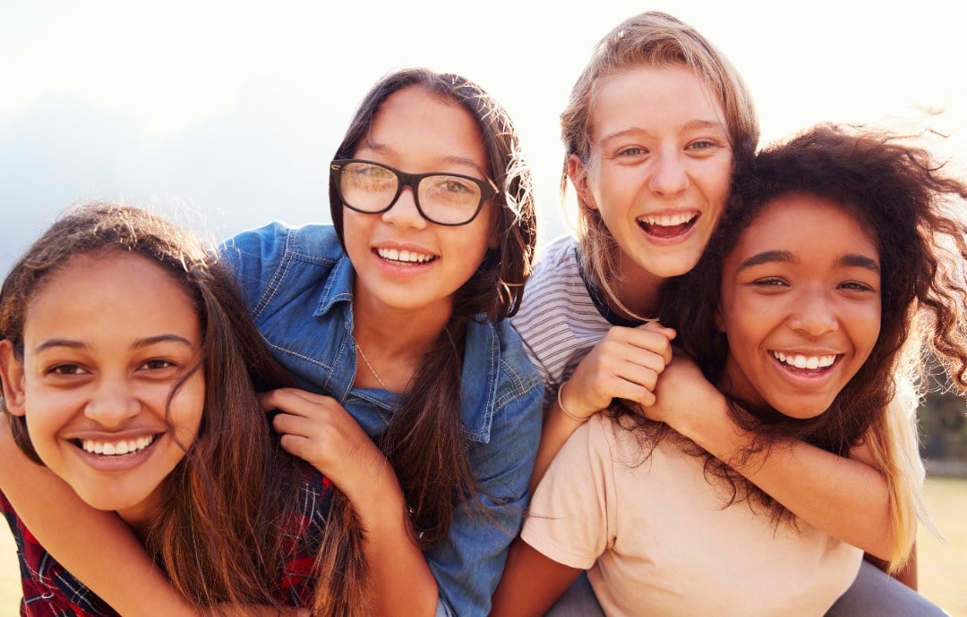 A group of four diverse teen girls, smiling at the camera.